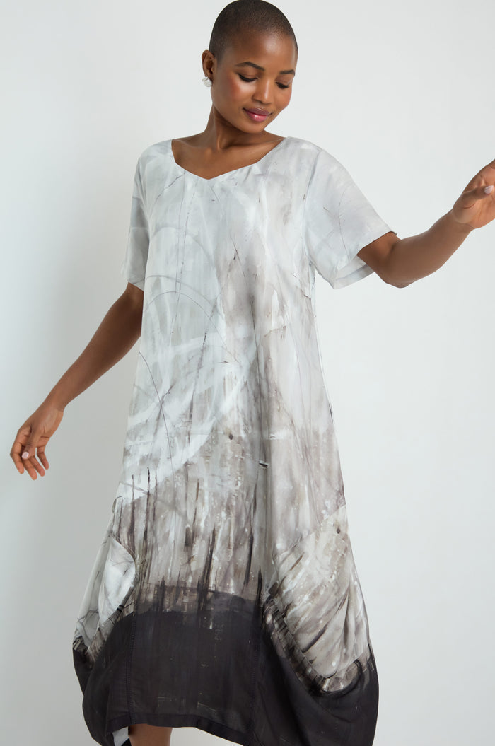 A woman with long white hair models the Abstract Print Bubble Dress, featuring a relaxed fit, short sleeves, and a gray-and-black abstract pattern, standing against a plain white background.