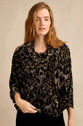 A woman with long red hair stands against a beige background wearing the Animal Print Cowl Neck Velvet Top, a loose-fitting black and brown velvet piece.