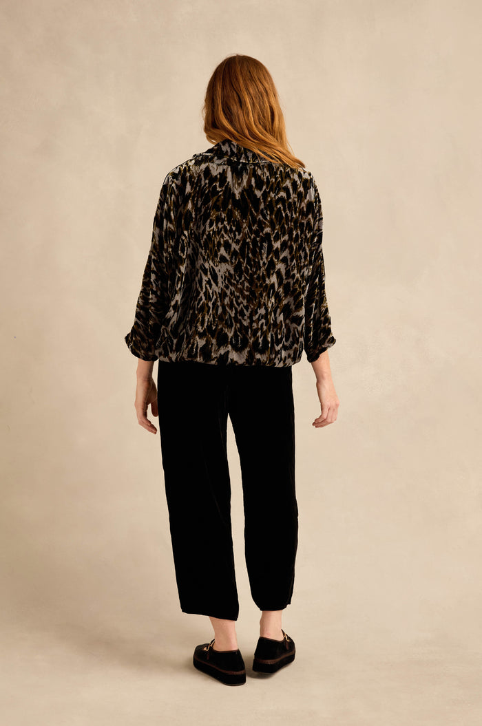 A person with long hair is seen from behind, wearing a patterned jacket layered over the Animal Print Cowl Neck Velvet Top, paired with black pants and black shoes, standing against a neutral background.