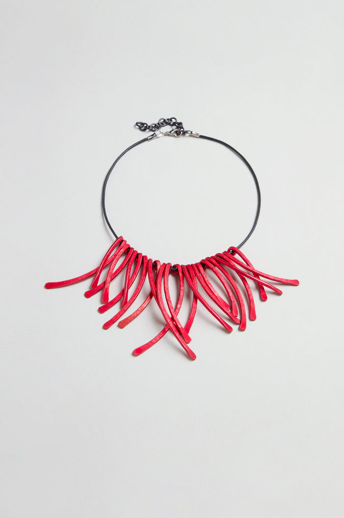 Introducing the Arc Necklace: a black choker featuring multiple curved red anodised aluminium elements fanned out at the front, secured with an adjustable metal clasp closure. This contemporary jewellery piece is crafted as wearable art, making a bold and striking statement.