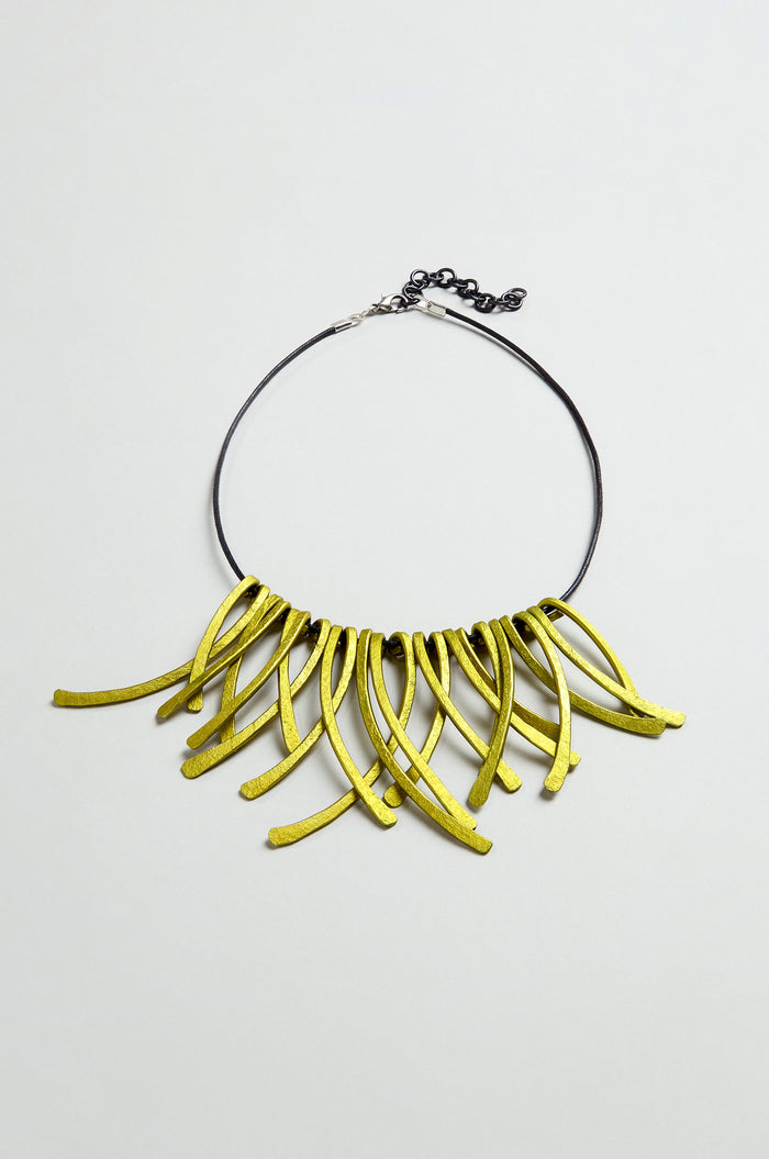 Discover the Arc Necklace: a striking piece of contemporary jewellery that serves as wearable art. Featuring a black chain and multiple curved, yellow-green pendants arranged in a dramatic fringe pattern, this necklace is expertly crafted from anodised aluminium to blend modern style with artistic flair.