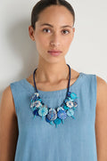 A woman in a sleeveless light blue dress wears the Azure Short Disc Necklace, featuring striking patterned circular elements, as she stands against a plain light background.