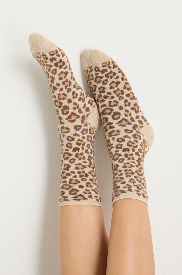 A pair of feet wearing Bamboo Leopard Print Socks with a beige, brown, and black pattern, set against a plain white background.