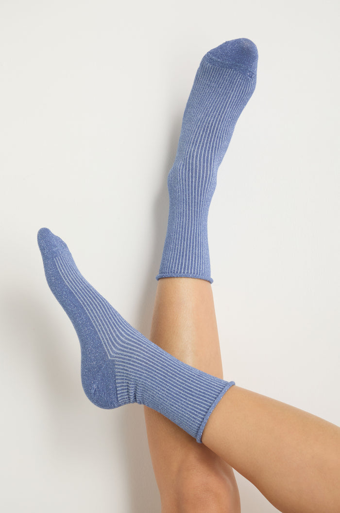 Someone wearing Bamboo Sparkle Blue Socks sits with crossed legs against a plain white background.