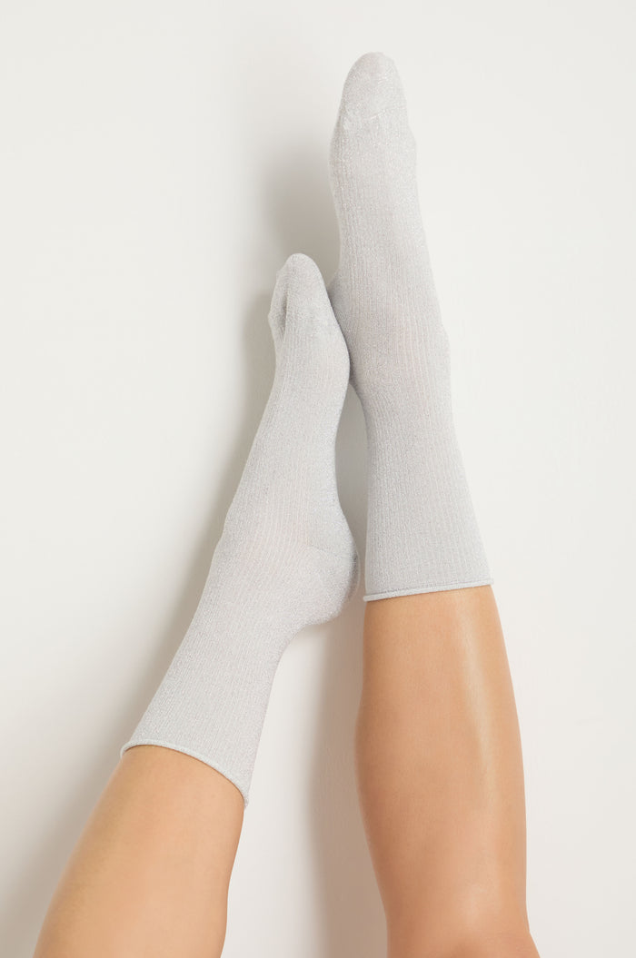 Two legs extended upward, wearing Bamboo Sparkle Cloud Socks in light gray metallic lurex, set against a plain white background.