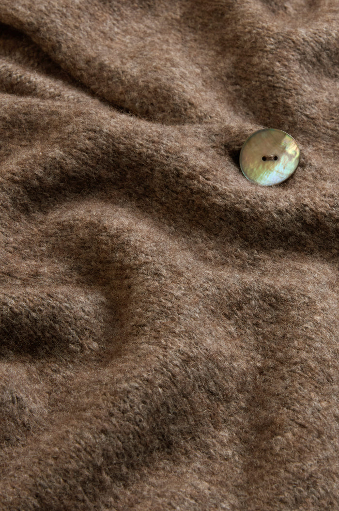 Close-up of a brown woolen fabric from the Bark Alpaca Blend Long Line Cardigan, featuring a single iridescent round button sewn near the upper right corner—a perfect detail from this women’s knitwear piece.