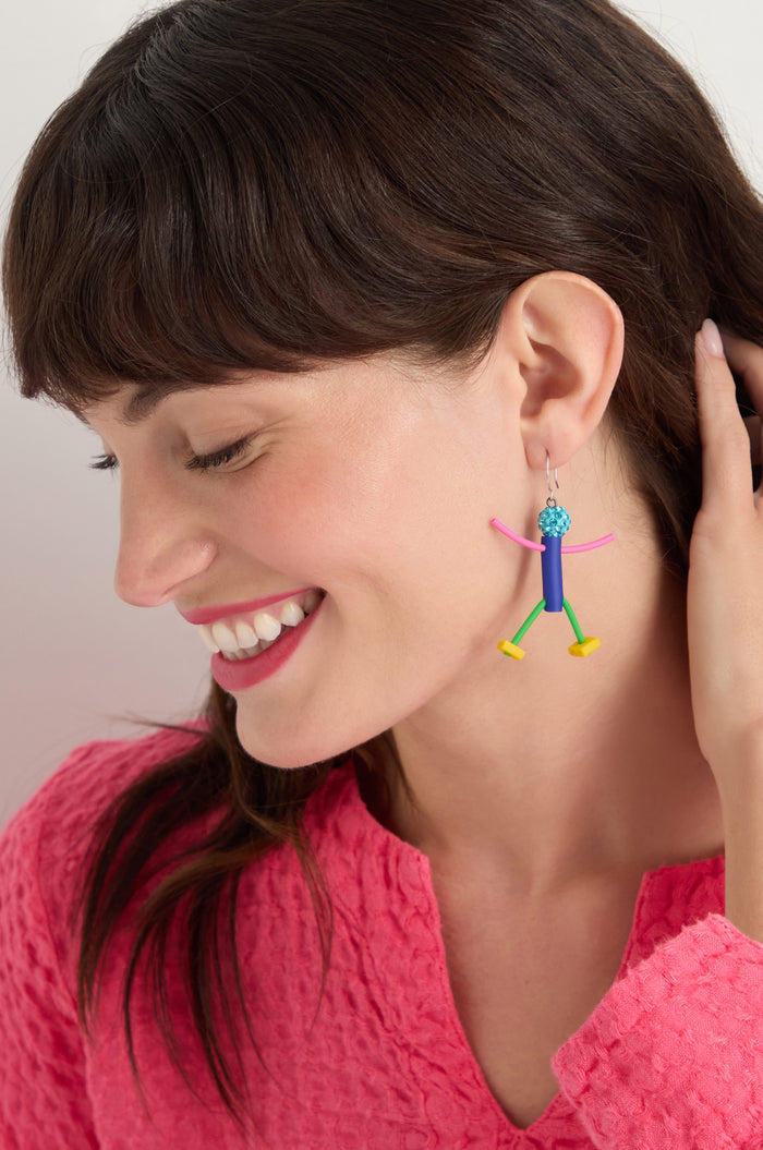 A woman with brown hair smiles, wearing a bright pink textured top and the Beautiful People Earrings—colorful, abstract, handmade in Paris—for a charming, playful touch while she holds a hand near her ear.