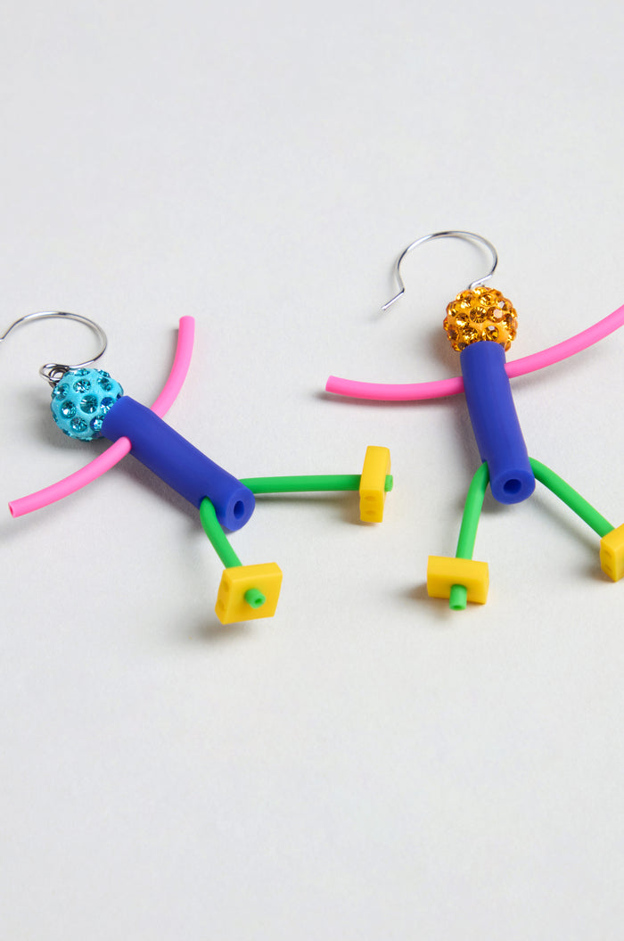 Beautiful People Earrings—handmade in Paris from beads and plastic tubing in blue, pink, yellow, and green—feature two colorful stick figure shapes displayed on a plain light background.