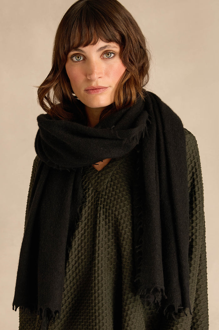 A woman with shoulder-length brown hair, dressed in a textured dark green top and wrapped in the Black Soft Cashmere Scarf, stands against a neutral background.