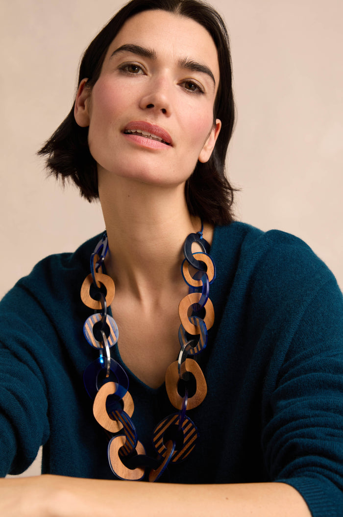 A woman with short dark hair, wearing a teal sweater and the Blue Stripe Wooden Resin Links Necklace, poses against a neutral background.