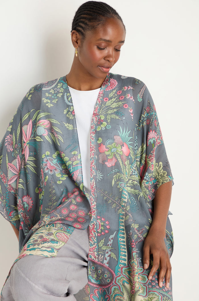 A woman wearing the Boho Garden Print Throwover over a white top and light gray pants looks down with a neutral expression.