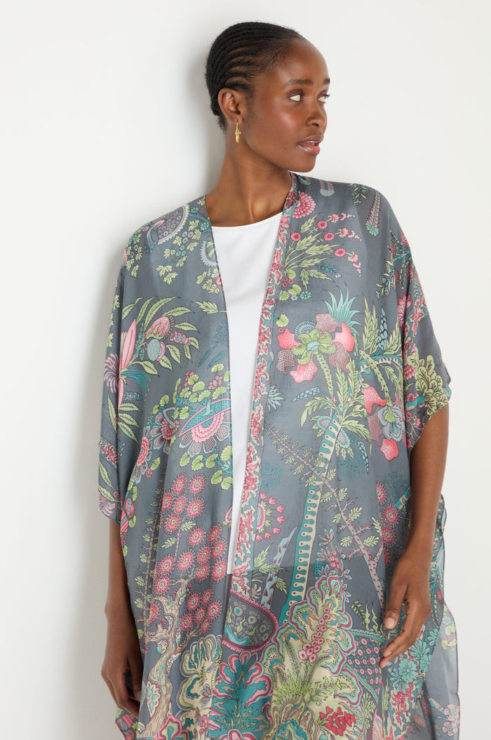 A woman wearing a Boho Garden Print Throwover over a white top stands against a white background, looking to the side.