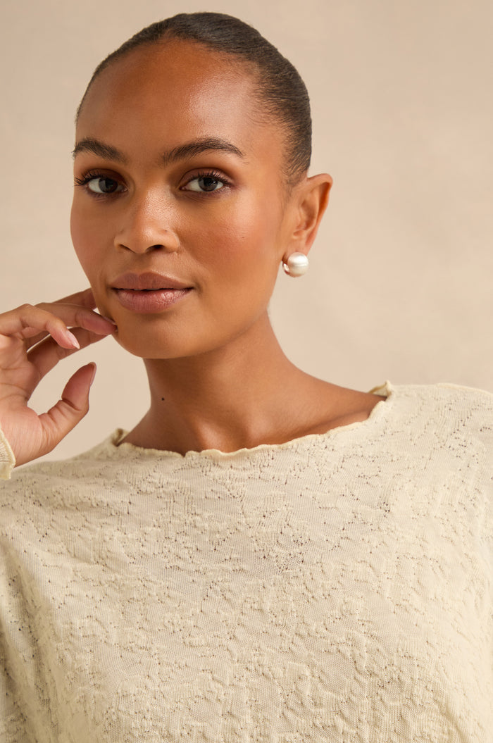 Woman wearing a cream textured top and the Brushed Sphere Earrings, with her hair pulled back, looking at the camera with her hand near her face.