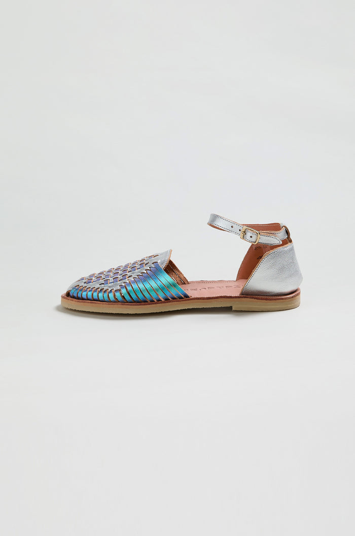 The Camila Mermaid Woven Sandals feature a multicolored woven leather upper, closed toe, metallic silver heel, and ankle strap with buckle. This flat style is an online exclusive, shown in profile on a plain background.