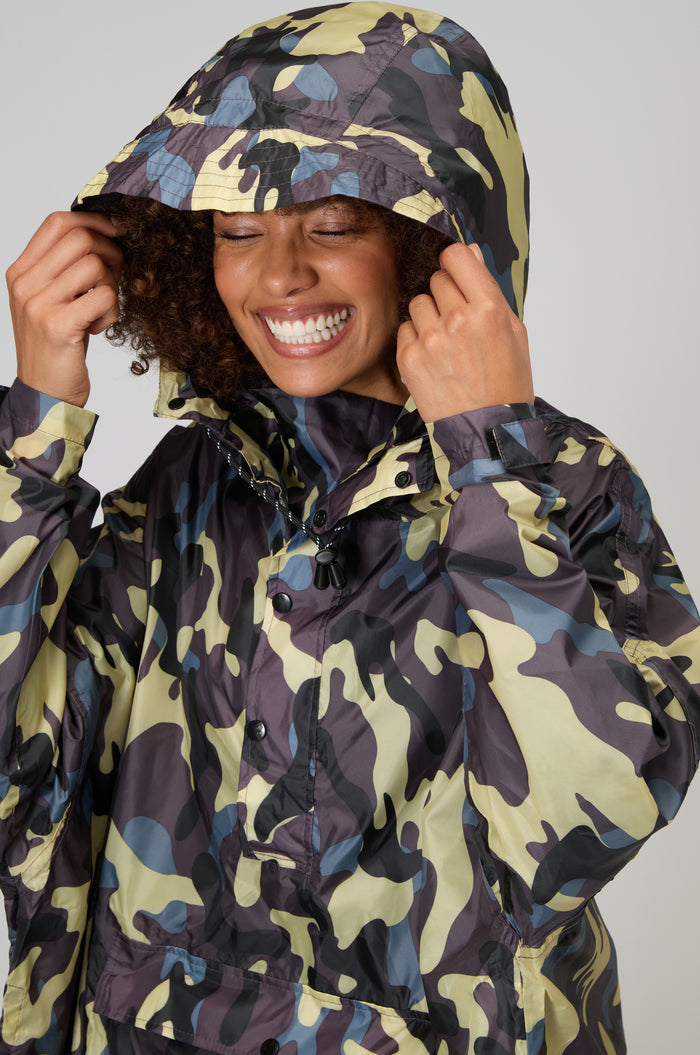 Smiling, a person adjusts the hood of the Camo Poncho, enjoying the comfort and style of this waterproof poncho.