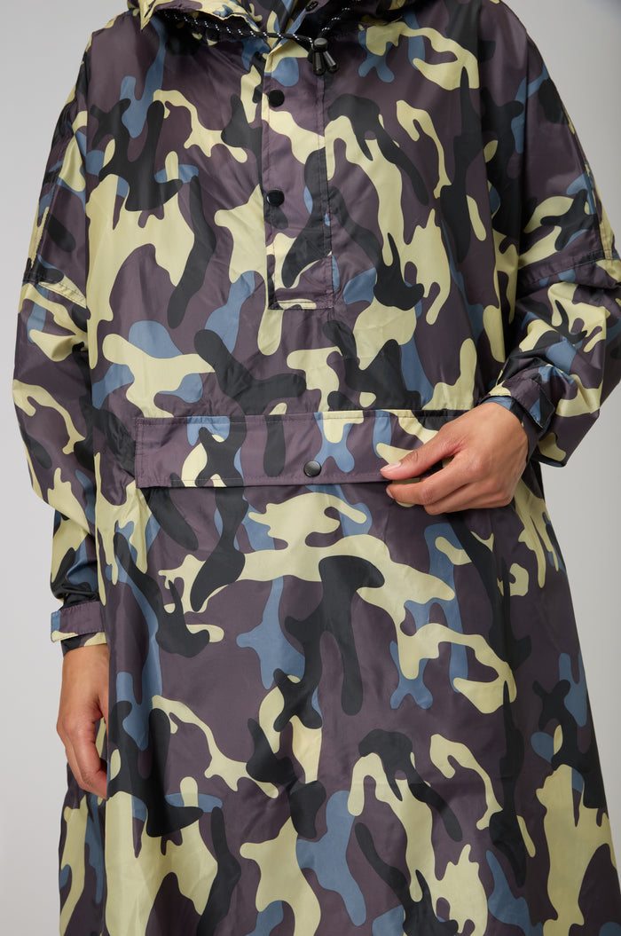 Staying dry and stylish, a person in the Camo Poncho with hood holds the front pocket flap, showing off this waterproof design.