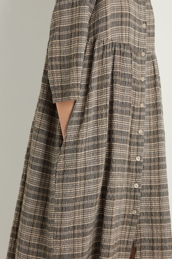 Side view of a person wearing the Check Button-Through Taupe Dress, a loose, short-sleeve textured cotton dress with pockets, highlighting Danish design.
