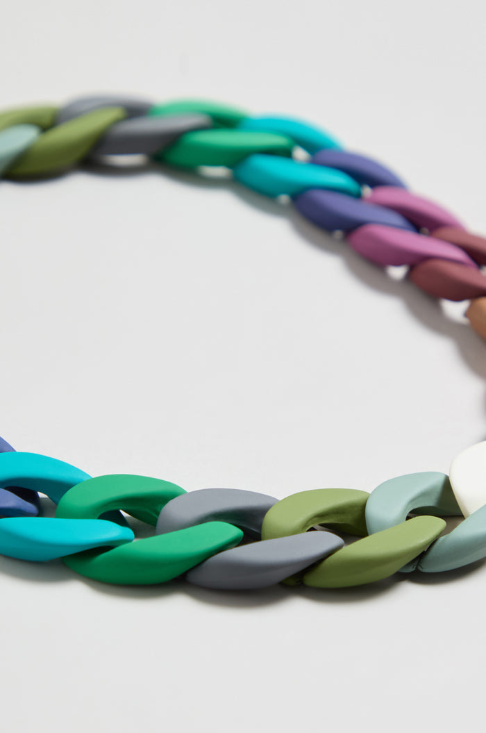 A close-up of the Colour Pop Link Necklace, a bold accessory with chunky links in green, blue, gray, purple, and beige displayed on a white background.