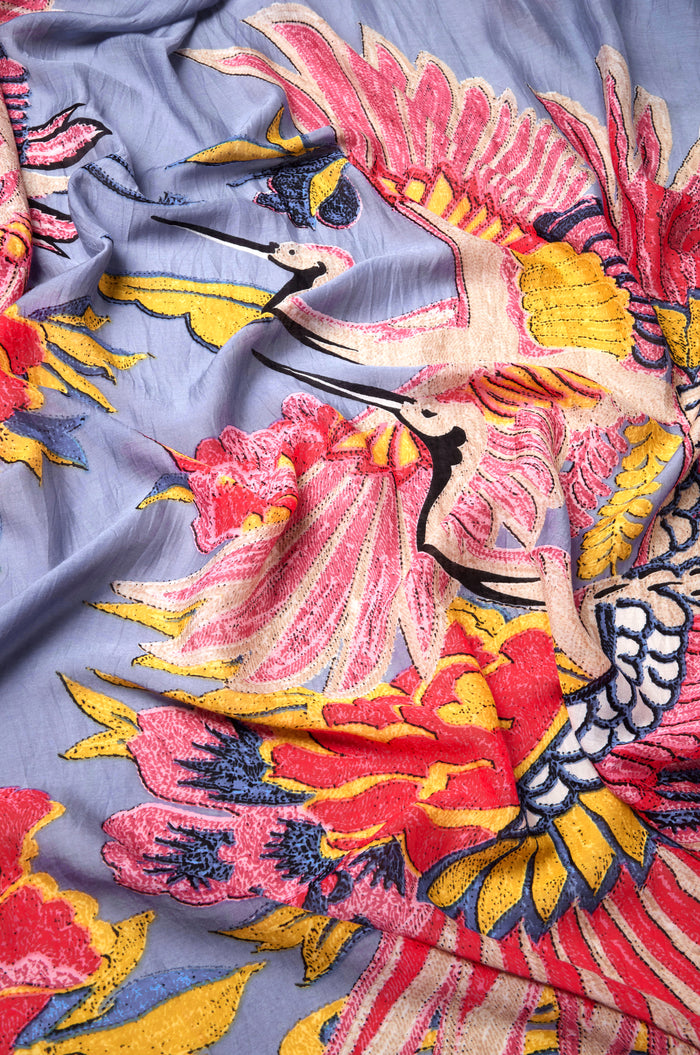 A close-up of the Crane Print Scarf, made from sustainable blue fabric and showcasing vibrant embroidered cranes with large pink, yellow, and red flowers.