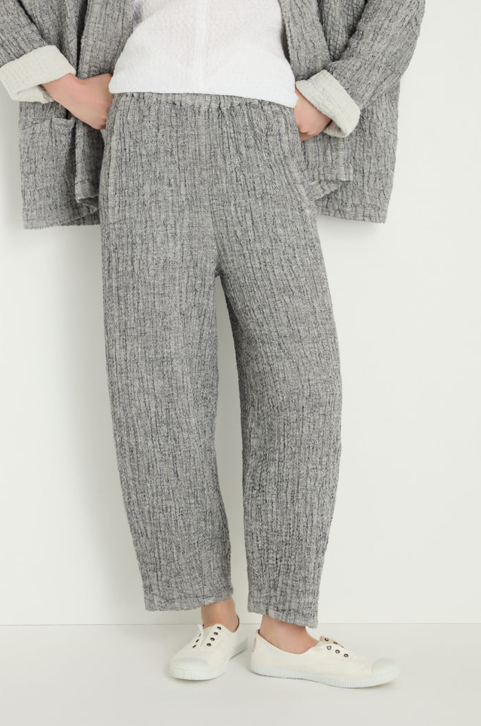 A person wears the Crinkle Double Face Linen Bubble Trouser in gray with a relaxed bubble fit, paired with a matching gray jacket, white top, and white sneakers, standing against a plain white background.