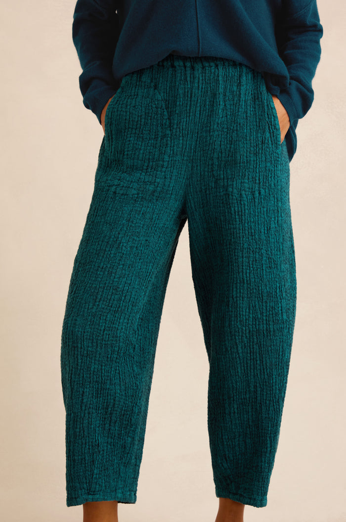 Model wearing Crinkle Linen Blend Bubble Trousers in teal, hands in pockets, shown from torso to feet against a plain background.