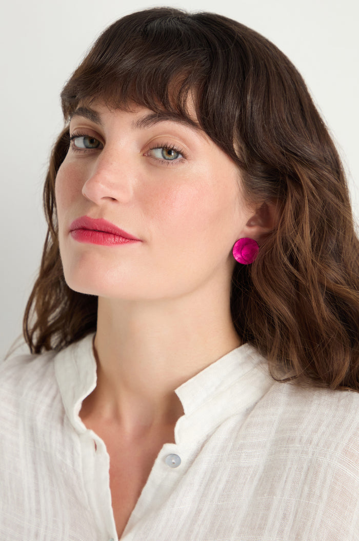 Woman with wavy brown hair wears a white textured blouse and bright pink Curved Disc Earrings, featuring anodised aluminium and sterling silver posts, as she looks slightly to the side against a plain background.