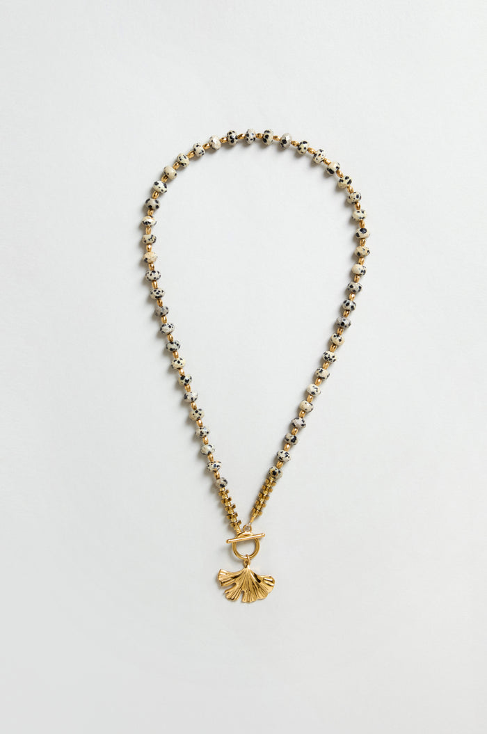 The Dalmatian Stone Ginkgo Leaf Necklace features gold and silver beads, a textured ginkgo leaf pendant, and a toggle clasp, displayed on a flat neutral background.