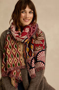A woman smiles at the camera against a neutral background, wearing a brown sweater and the Embroidered Cotton Wool Scarf, which is adorned with vibrant red, green, and cream geometric and floral motifs. The scarf features delicate fringed edges for an added touch of elegance.