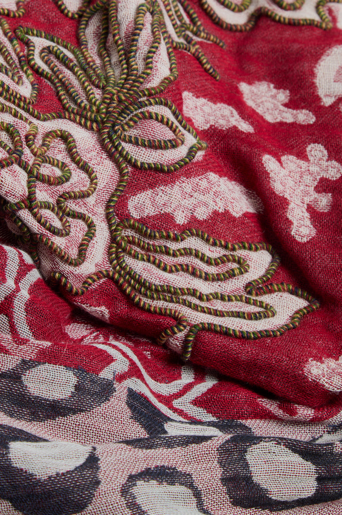 Close-up of the Embroidered Cotton Wool Scarf, showcasing vivid red fabric adorned with intricate green, white, and black embroidery in geometric floral motifs and abstract patterns. This beautiful scarf is elegantly finished with delicate fringed edges.