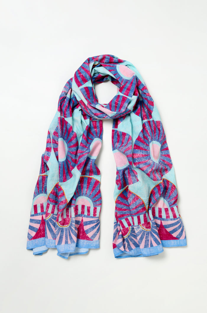 The Embroidered Parasols Cotton Scarf features a blue background with pink, red, and light blue geometric sunburst patterns inspired by parasols, displayed flat on a white surface.