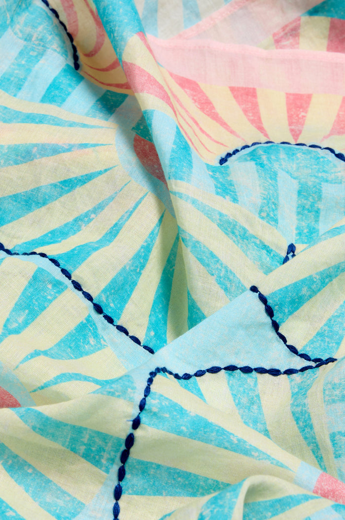 Close-up of the Embroidered Parasols Cotton Scarf, showcasing a pastel sunburst pattern in blue, yellow, and pink with dark blue stitched lines and parasol-inspired details.