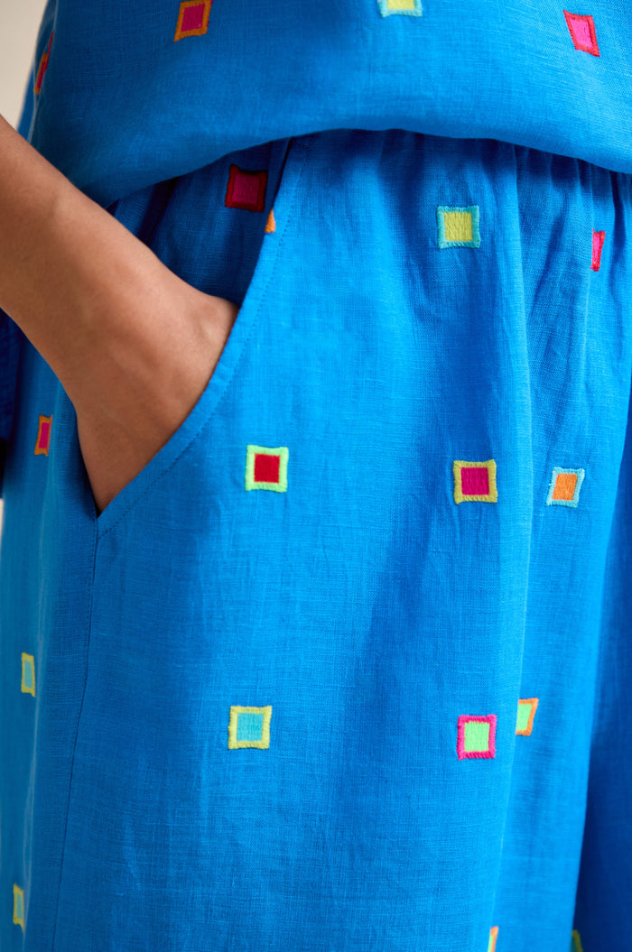 A close-up of a hand in the pocket of Embroidered Squares Linen Wide Trousers, featuring colorful embroidery, a wide fit, and a modern cropped length.