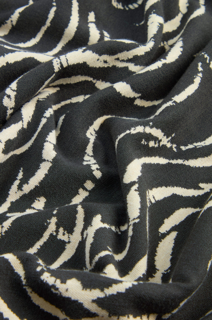 Black stretch jersey fabric with white, wavy, abstract lines forms a flowing wave motif across the Dancing Waves Zip Boxy Jacket. The material has a soft feel and a slightly crumpled texture, making it ideal for this relaxed, boxy jersey jacket.