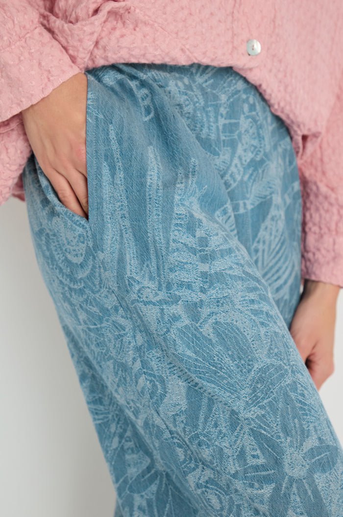 A person wears the Floral Jacquard Cotton Bubble Trouser in blue with a pink textured shirt, one hand in their pocket.