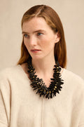 A woman with long brown hair wears a cream sweater and the Flower Bead Necklace, which features collar-length flower beads with gold accents, as she looks slightly to the side against a neutral background.