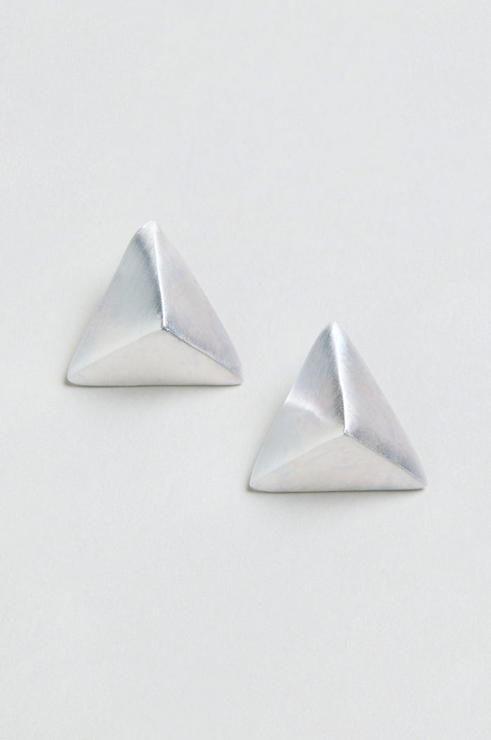 Two silver Folded Triangle Earrings, each featuring a pyramid-shaped geometric design, are displayed against a plain, off-white background.