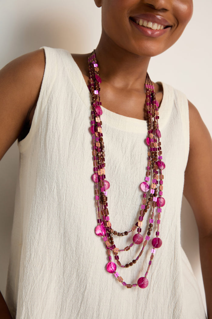 Woman wearing a sleeveless cream top and the Four Strand Sequin Necklace, a stylish layered piece featuring reflective sequins in shades of pink and brown, smiling slightly.