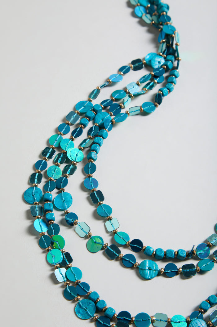 The Four Strand Sequin Necklace features multiple strands of sparkling sequins in various shapes and sizes, arranged in parallel lines to create a bold layered look, beautifully displayed on a light surface.
