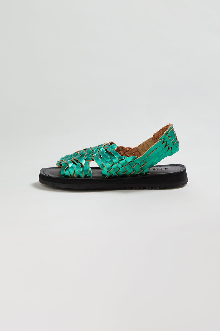 Frida Metallic Green Leather Sandals—handcrafted in Mexico with an open toe and heel, flat black sole, and intricate woven pattern—are showcased against a plain white background.