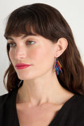 Woman with brown hair and bangs wears Fringe Earrings made from anodised aluminium in rainbow drops, paired with a black top, looking to the side against a plain background.