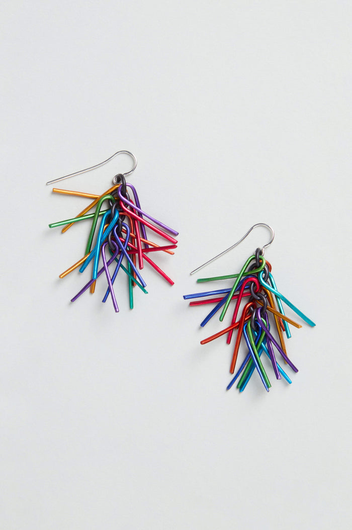 Fringe Earrings featuring clusters of thin, colorful anodised aluminium rods in red, blue, green, purple, and yellow are arranged in a vibrant rainbow fringe on silver hooks.