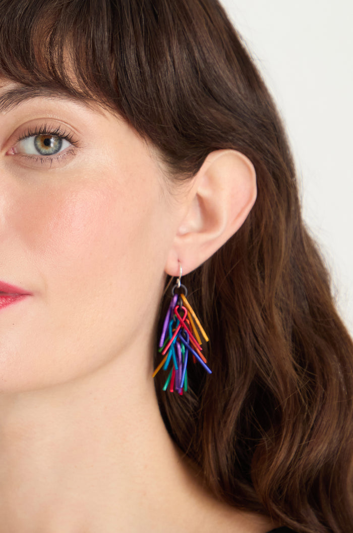 Close-up of a woman with wavy brown hair wearing Fringe Earrings, featuring several thin, curved pieces for a vibrant look. Only the left side of her face is visible.