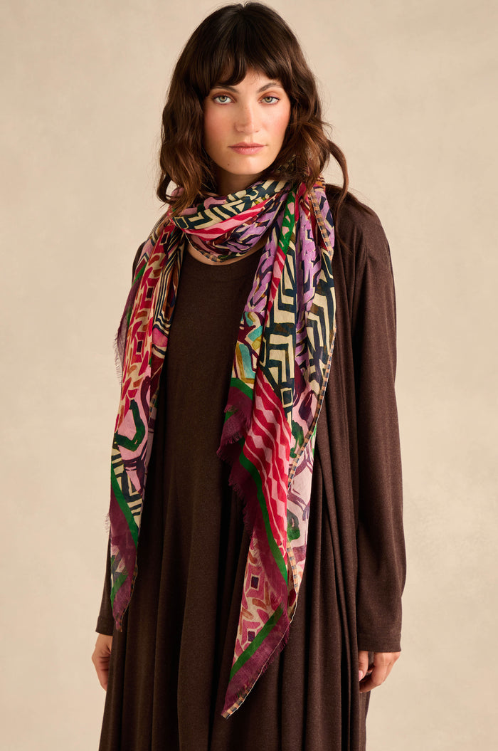 A woman wearing a long brown dress and the Graphic Print Wool Scarf stands against a neutral background, looking at the camera.