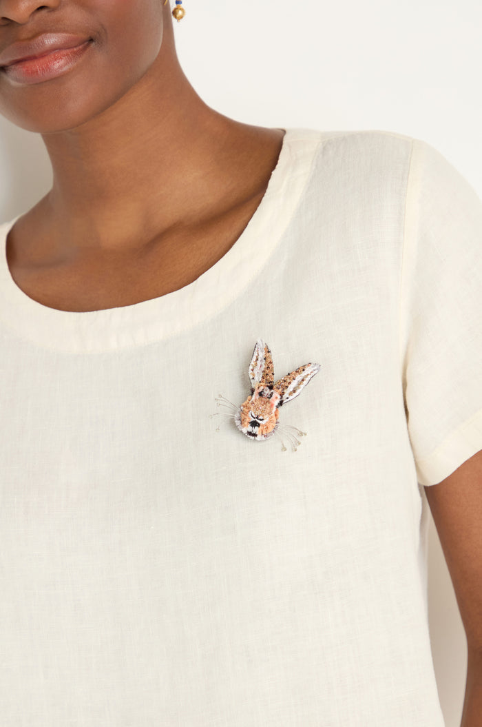 A woman wears a cream-colored top featuring the Hand Embroidered Bunny Rabbit Brooch on her chest.