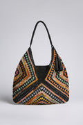 The Handwoven Bohemian Raffia Bag features a large, multicolored geometric patchwork design with a black handle and tassel, shown against a plain background.
