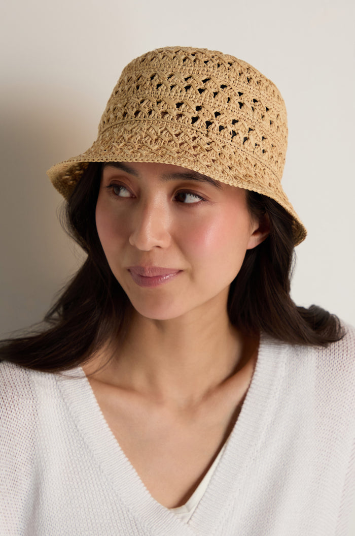 A woman with long dark hair wears the Handwoven Raffia Bucket Hat, facing slightly to the side in a neutral setting.