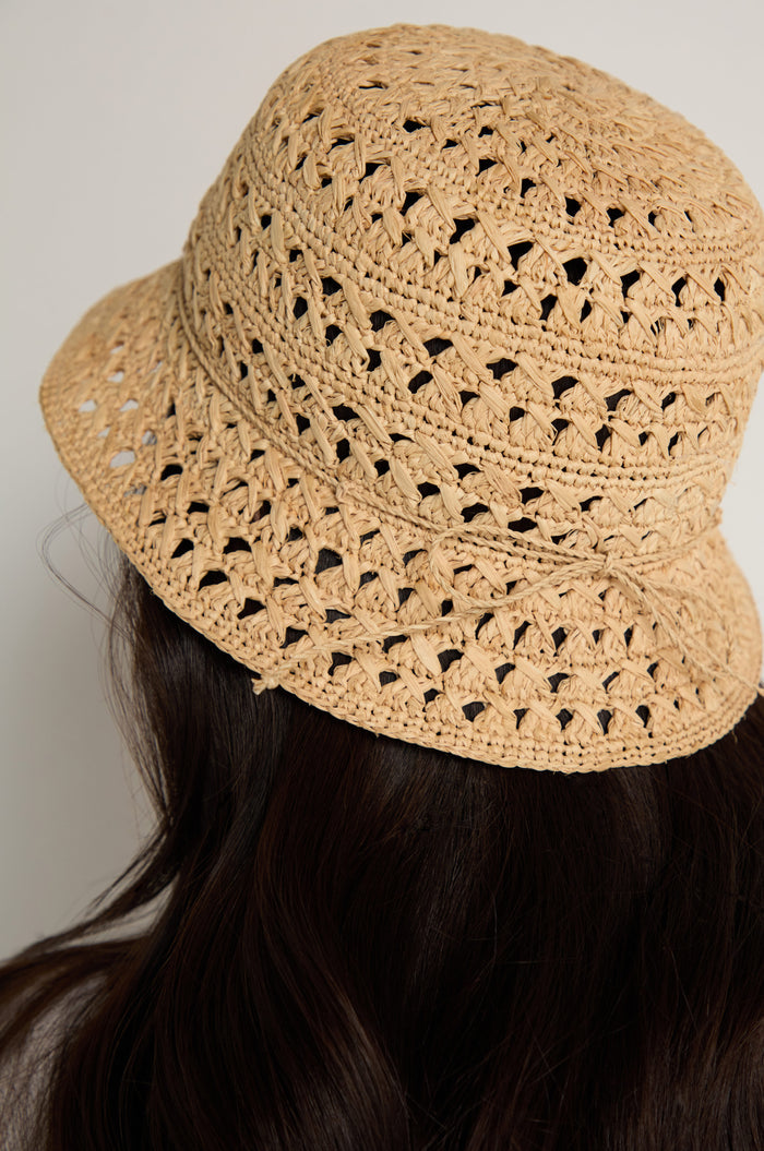 Someone with long, dark hair is shown from behind wearing the Handwoven Raffia Bucket Hat against a neutral background.