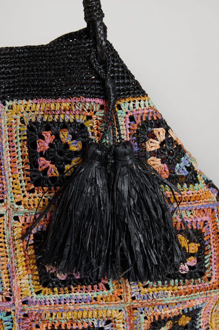 Close-up of the Handwoven Raffia Crochet Bag from Madagascar, showcasing a colorful patchwork crochet design and two black raffia tassels by the handle.