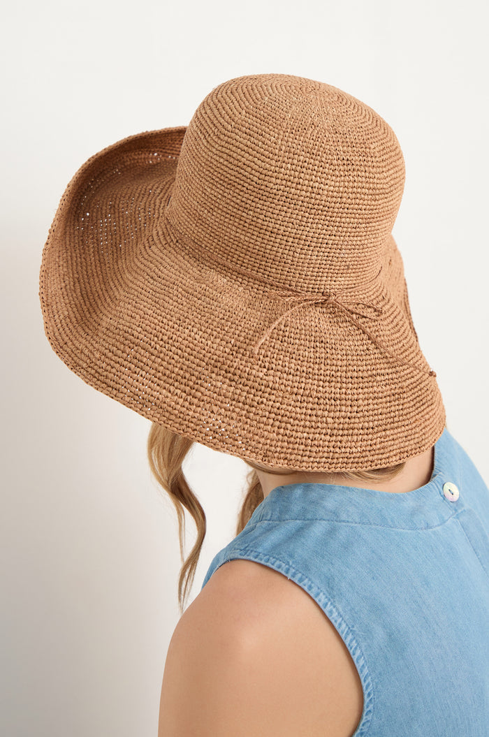 A person faces away from the camera, wearing a Handwoven Raffia Tie Hat with a wide brim and a sleeveless light blue top.