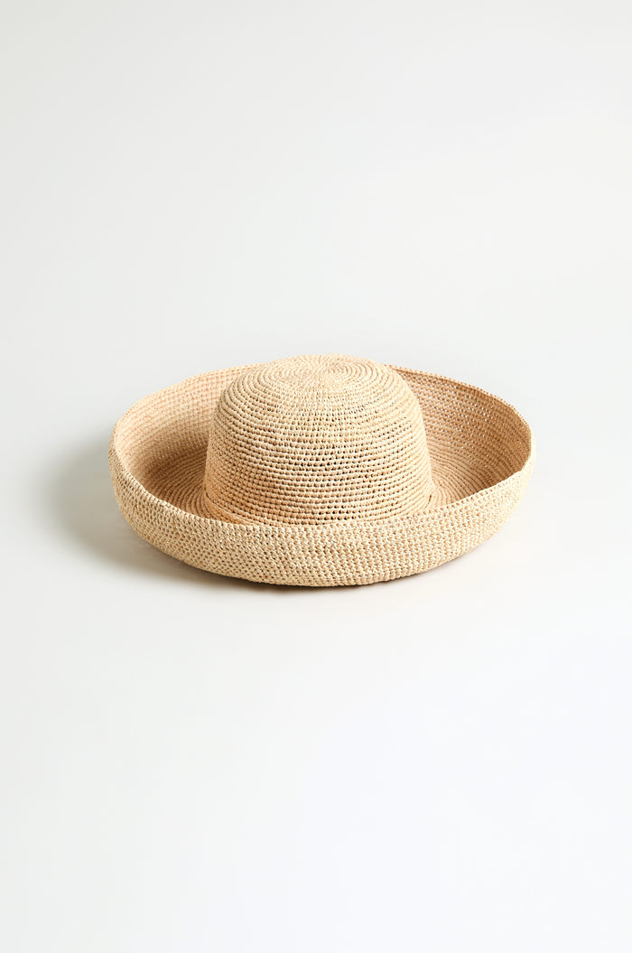 The Handwoven Raffia Tie Hat features a wide, flat brim and rounded crown, handwoven from natural raffia and shown against a plain white background.